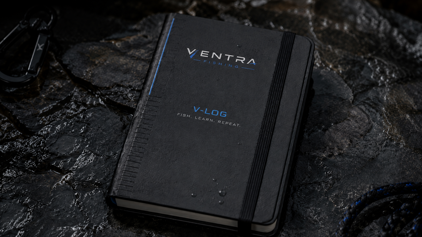 V-LOG fishing field journal, dark cover with Ventra Fishing mark, resting closed on wet rock